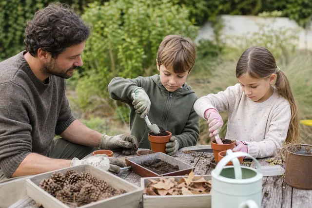 Enfants accompagnés semant des graines dans des pots au jardin.