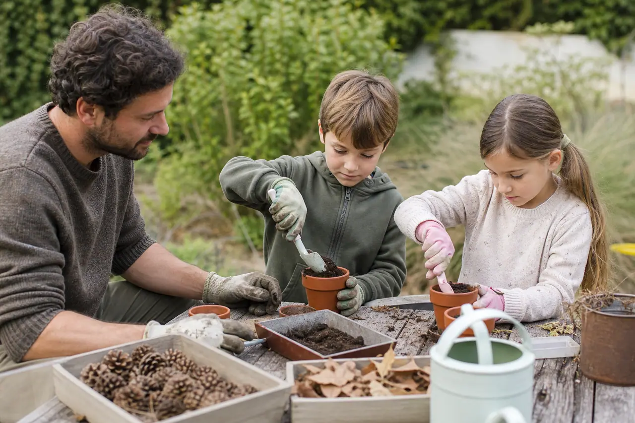 Enfants accompagnés semant des graines dans des pots au jardin.