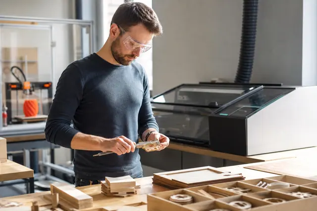 Personne mesurant une pièce en bois dans un atelier de fabrication partagé.