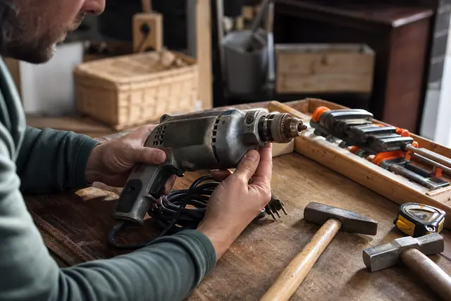 Particulier contrôlant une perceuse filaire d’occasion sur un établi en bois.