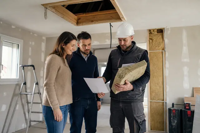 Couple et artisan préparent un projet d’isolation dans une maison rénovée.