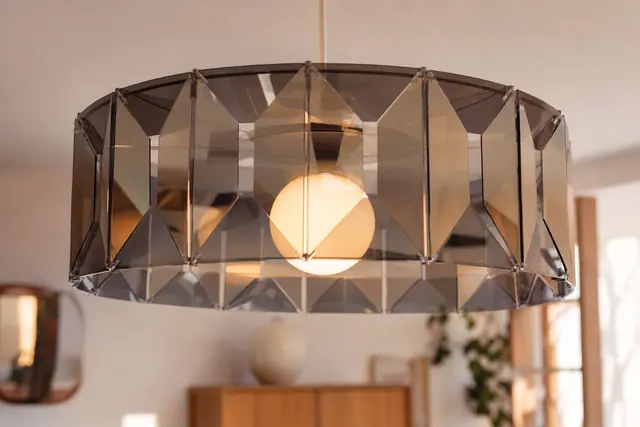 Suspension glossy ajourée en panneaux miroir au-dessus d’une table en bois.