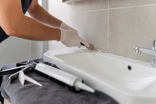 Locataire refaisant soigneusement un joint de silicone autour d’un lavabo