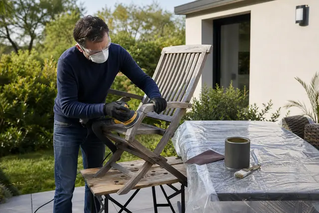 Personne équipée ponçant une chaise en bois dans un jardin.