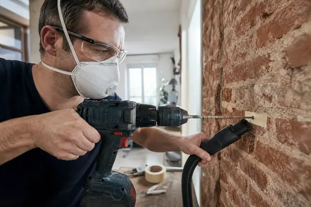 Bricoleur équipé perçant soigneusement un mur de brique avec une perceuse-visseuse.