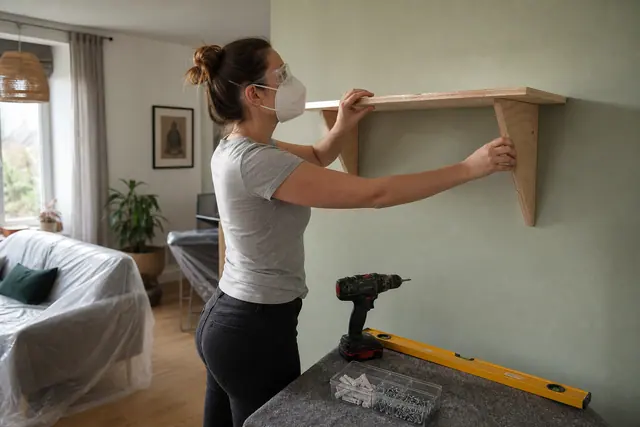 Bricoleuse installant une étagère en bois dans un salon lumineux