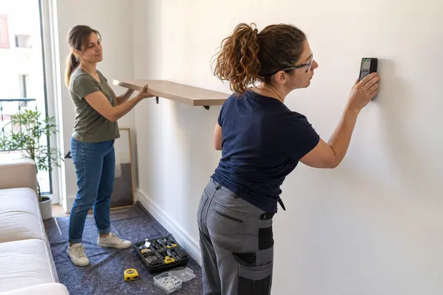 Intervenante vérifiant un mur avant de poser une étagère chez une cliente.