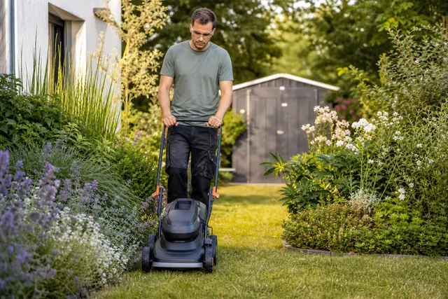 Jardinier tondant une pelouse sèche avec une tondeuse sur batterie compacte.