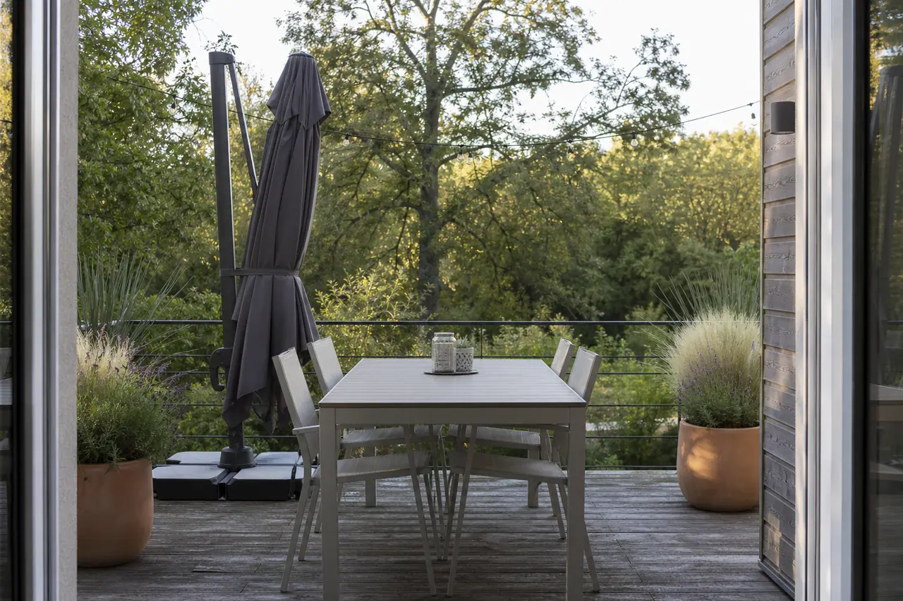 Terrasse aménagée avec table, parasol lesté, pots végétalisés et éclairage discret