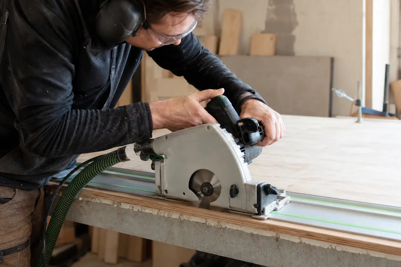 Découpe sécurisée d’un panneau sur rail avec lunettes, casque et serre-joints.