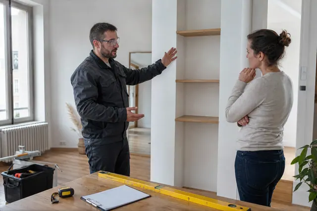 Bricoleur et propriétaire vérifiant une pose d’étagère dans un appartement lumineux.