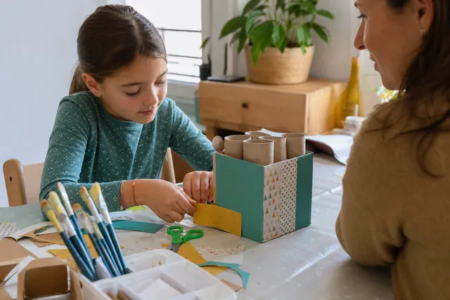 Enfant décorant un organiseur en carton recyclé sur une table protégée.