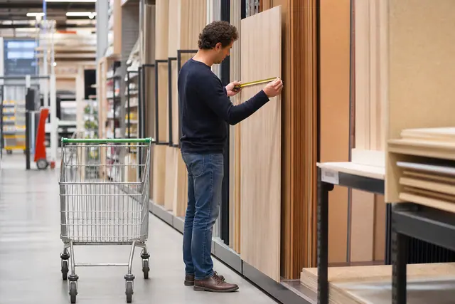 Client mesurant un panneau de bois dans un magasin de bricolage.