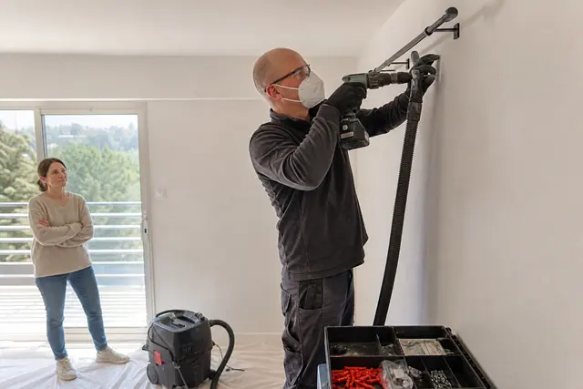 Intervenant équipé fixe une tringle dans un appartement avec aspiration des poussières.