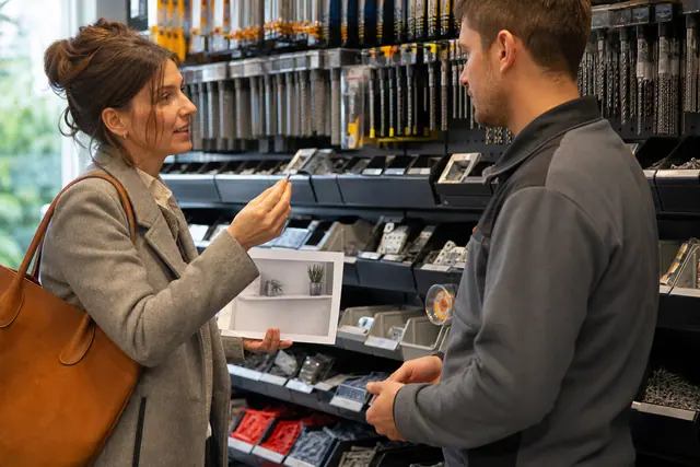 Cliente échangeant avec un conseiller devant un rayon de quincaillerie de proximité.