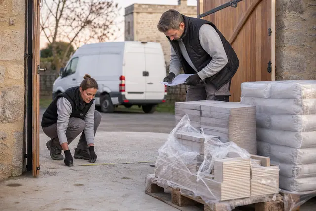 Couple mesurant l’accès du chantier avant une livraison de matériaux sur palette.