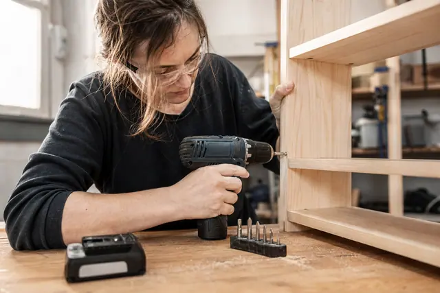 Bricoleuse utilisant une perceuse-visseuse sans fil pour assembler une étagère en bois.
