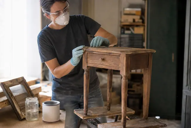 Préparation sécurisée d’un petit meuble ancien en bois dans un atelier lumineux.