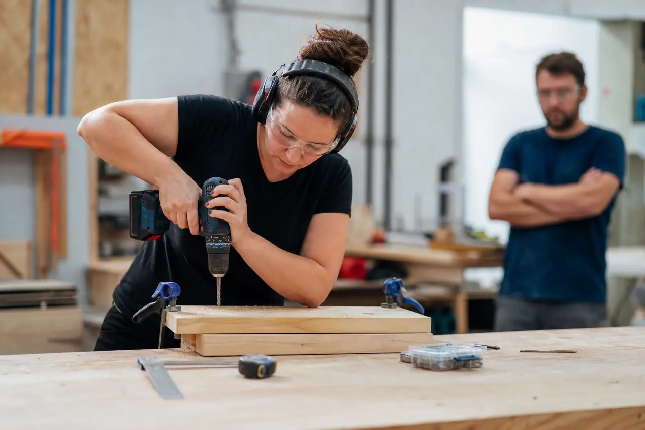 Débutante équipée utilisant une perceuse sur une planche serrée à l’établi.