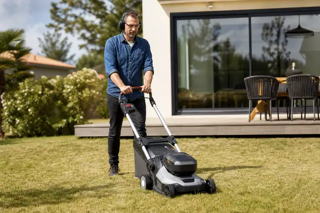 Particulier tondant une pelouse avec une tondeuse à batterie et protections