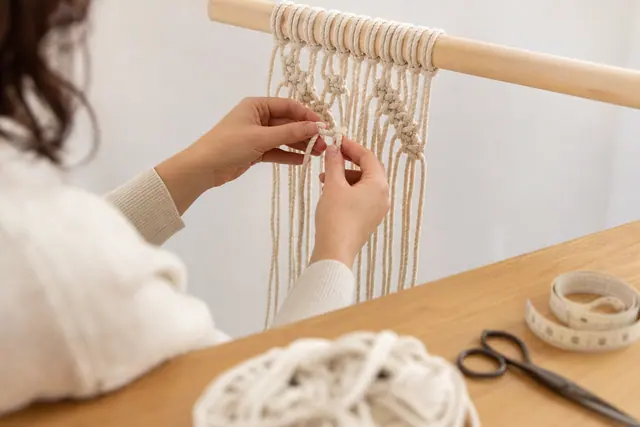 Débutante nouant une tenture en corde de coton sur une tringle en bois
